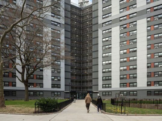 Two people walk towards a public housing building that has been renovated with a modern facade